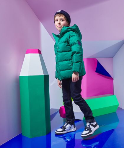 Ein Junge, im grünen Mantel mit schwarz-weißen Turnschuhen